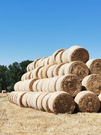 Stack of hay bales on field against clear blue sky