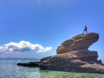 Man standing on rock against blue sky