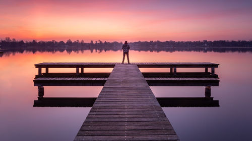 Silhouette man standing on pier over lake against sky during sunset