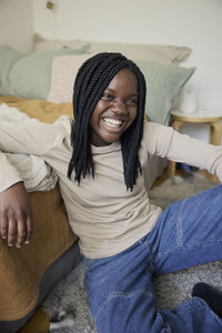 Happy teenage girl with braided hair sitting in bedroom at home