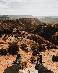 Low section of man sitting on rock against sky