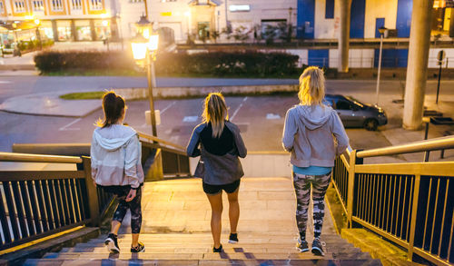 Women friends training running down stairs in city at night