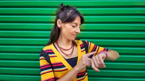 Smiling mature woman checking time against green 