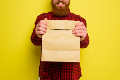 Midsection of man holding paper bag against yellow background