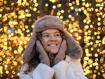 Portrait of young woman standing against illuminated christmas tree