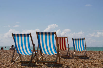 Deck chairs on beach against blue sky