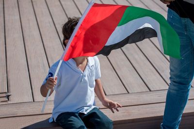 Boy holding flag in city during sunny day