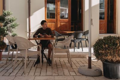 Portrait of young woman using mobile phone while sitting in front of house