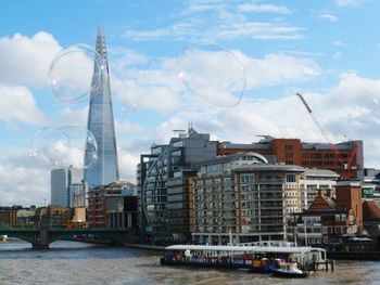 Soap bubbles over thames river in city against sky