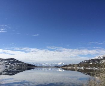 Scenic view of lake by snowcapped mountains against blue sky