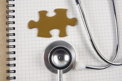 Directly above shot of stethoscope with jigsaw puzzle piece on notebook