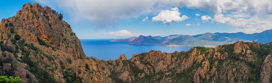 Panoramic view of rocky mountains by sea against sky