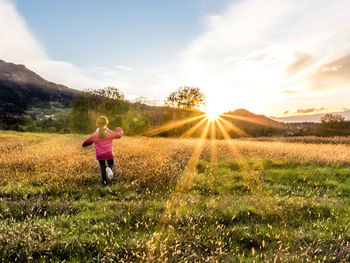Rear view of woman standing on field against sky during sunset