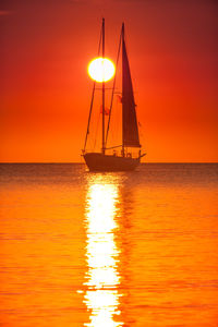 Sailboat in sea against orange sky