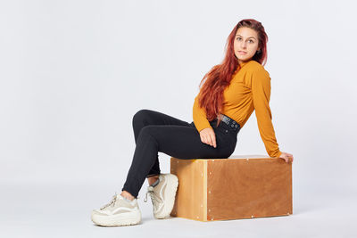Young woman in her twenties with orange clothes and red hair sitting in a wooden drawer
