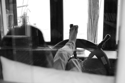 Low section of man with feet on helm in boat seen through glass