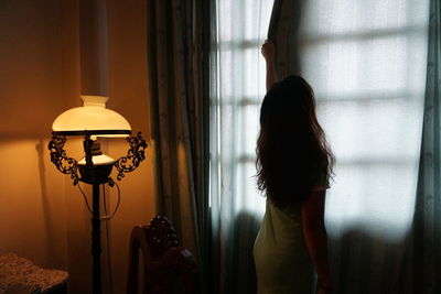 Rear view of woman closing curtain of window at home