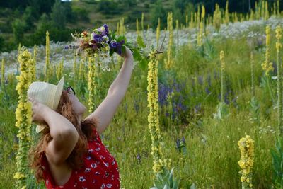 Rear view of girl holding flowering plants on field