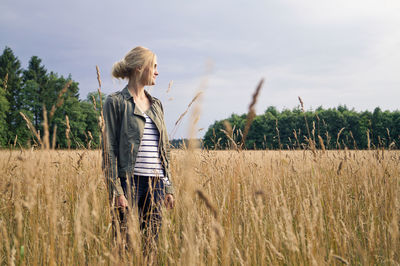 Young woman standing on grassy field against sky