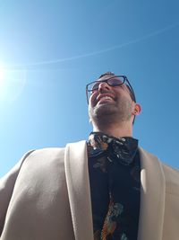 Low angle view of smiling businessman standing against blue sky