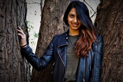 Portrait of smiling young woman standing against tree trunk