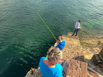 High angle view of sons fishing in sea while mother sitting on steps 