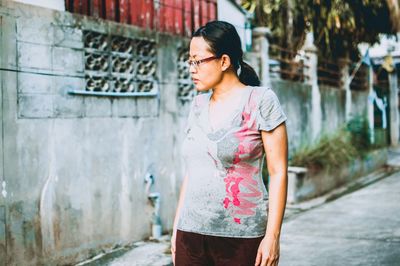 Young woman looking away while standing against wall