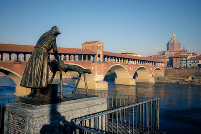 Statue by bridge against sky in city