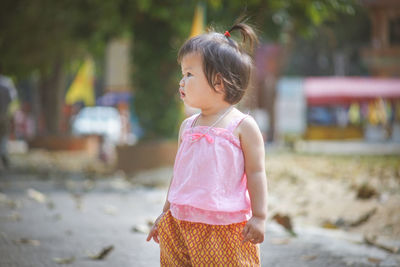 Cute baby girl looking away while standing on footpath