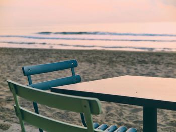 Chairs and table on beach against sky during sunset