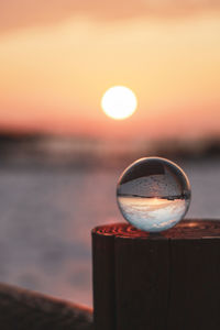 Close-up of glass against sea during sunset