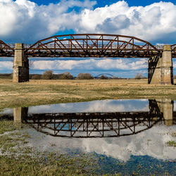 Reflection of railway bridge on puddle against sky