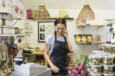 Happy woman talking on mobile phone while standing at counter in store