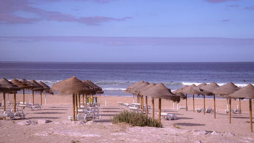 Lounge chairs and parasols on beach against sky