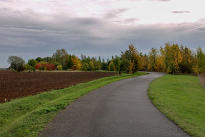 Road amidst trees on field against sky