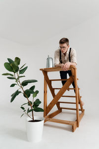 Man looking at plant while standing on ladder against white background