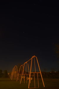 Low angle view of illuminated swings against sky at night