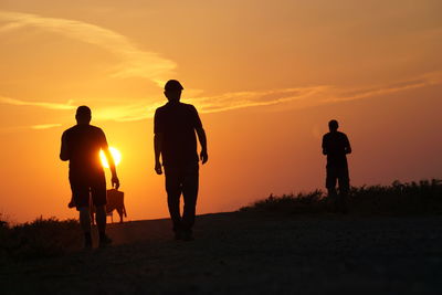 Silhouette men standing on land against sky during sunset