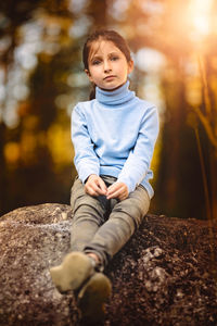 Cute boy looking away while sitting on rock