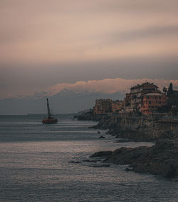 Sailboats on sea by buildings against sky during sunset