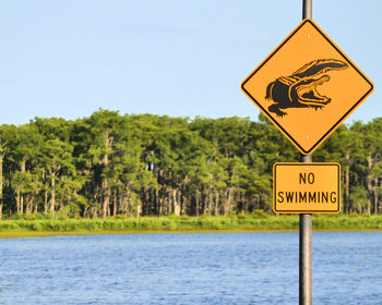 No swimming sign by lake against sky