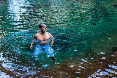 Young man swimming in natural waterfall clear water at morning from top angle