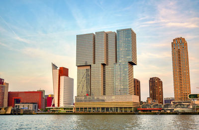 Modern buildings by river against sky in city