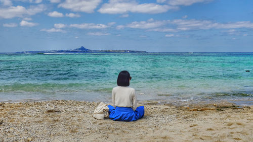 Rear view of woman sitting at beach against sky