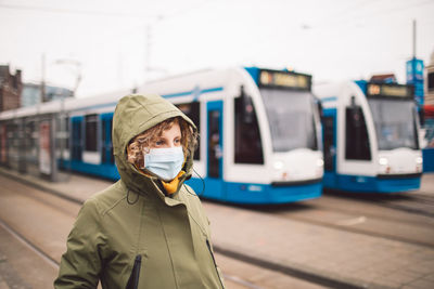 Woman wearing mask standing against trains