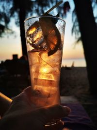 Close-up of hand holding drink against sky during sunset