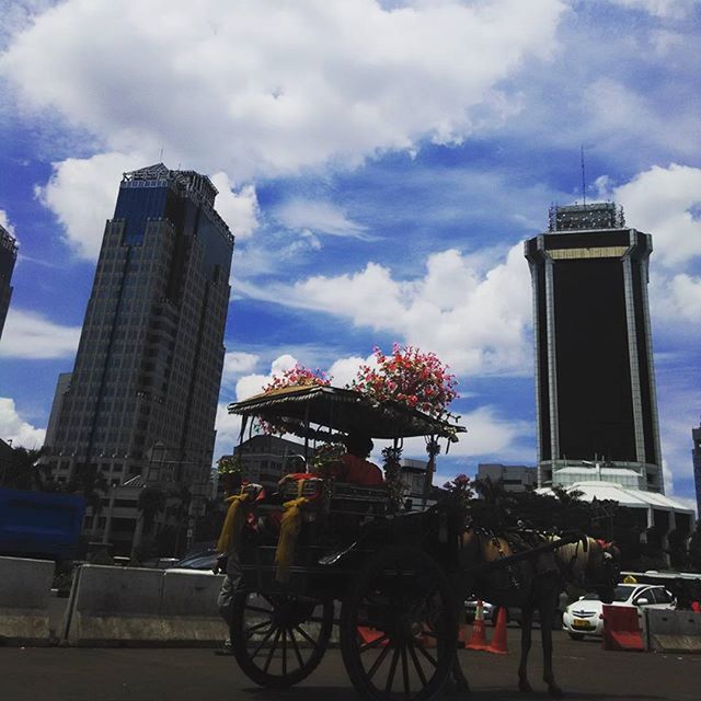 sky, building exterior, architecture, built structure, cloud - sky, land vehicle, transportation, cloudy, mode of transport, city, cloud, car, bicycle, tower, street, day, road, tree, outdoors, tall - high