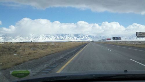 Road leading towards snowcapped mountains seen through car windshield