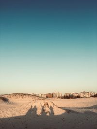 Shadow on people at beach against buildings and sky