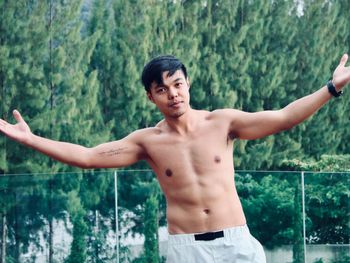 Young man with arms outstretched standing against plants